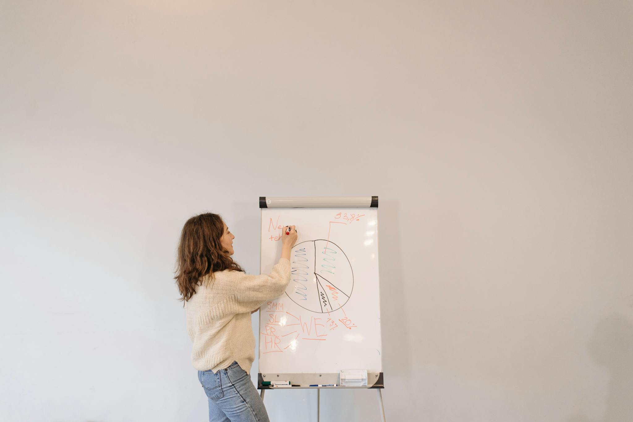 A woman with curly hair explains concepts using a whiteboard in an office. Professional and educational atmosphere.
